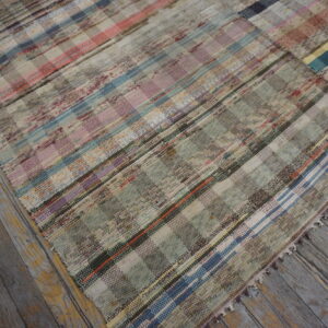 Flatweave rug in muted pink, blue, and green checkered stripes rests on distressed wood planks.