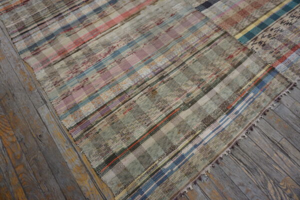 Flatweave rug in muted pink, blue, and green checkered stripes rests on distressed wood planks.