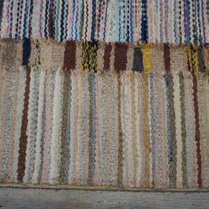 Textured rag rug with vertical neutral stripes below a patched band of bright multicolored weaving.
