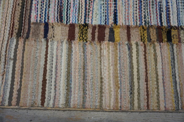 Textured rag rug with vertical neutral stripes below a patched band of bright multicolored weaving.