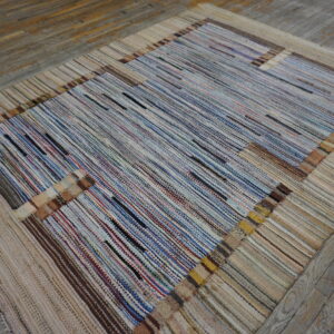 A multicolored striped rug with a wide neutral border lies on rustic wooden plank flooring.