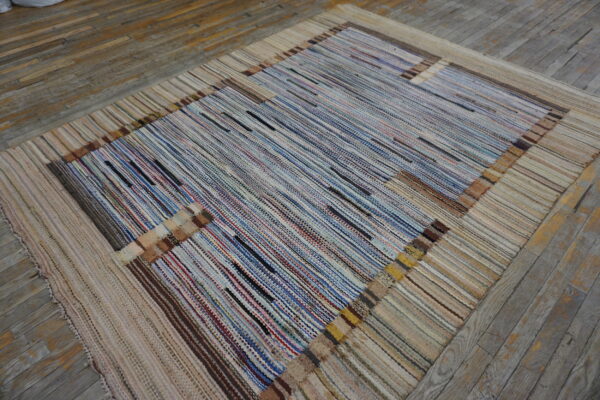 A multicolored striped rug with a wide neutral border lies on rustic wooden plank flooring.