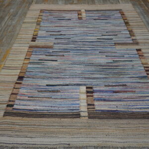 Blue and beige striped flatweave rug with a rectangular pattern lies on weathered gray wood.
