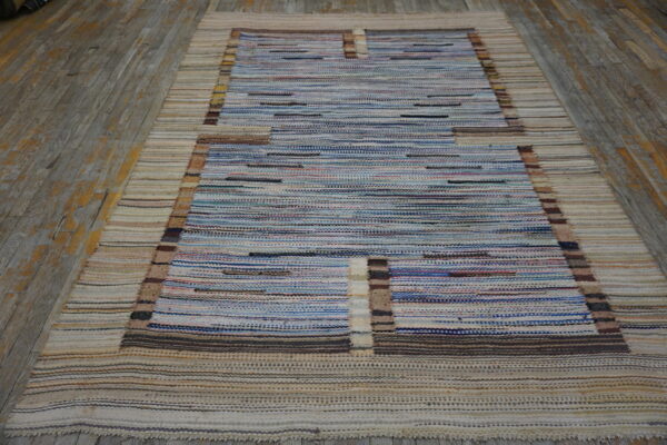 Blue and beige striped flatweave rug with a rectangular pattern lies on weathered gray wood.