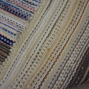 Textured braided rag rug with diagonal stripes in neutrals, gray, yellow, blue, and bright mixed colors.