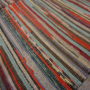 Multicolor striped rag rug with woven strips of red, teal, brown, and gray on wooden planks.