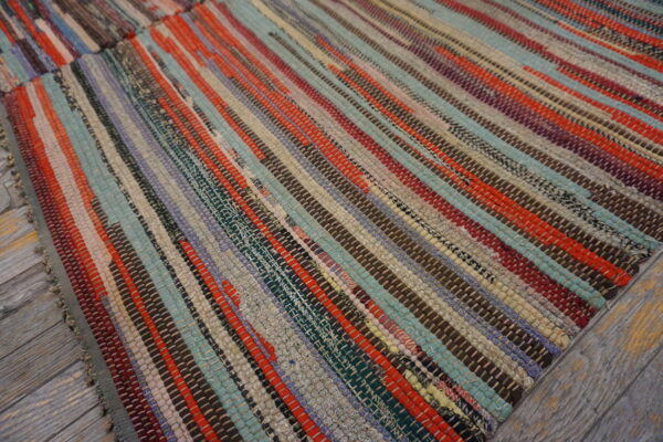Multicolor striped rag rug with woven strips of red, teal, brown, and gray on wooden planks.