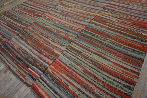 Multicolored striped flatweave rag rug with visible panel seams rests on rustic gray wood flooring.