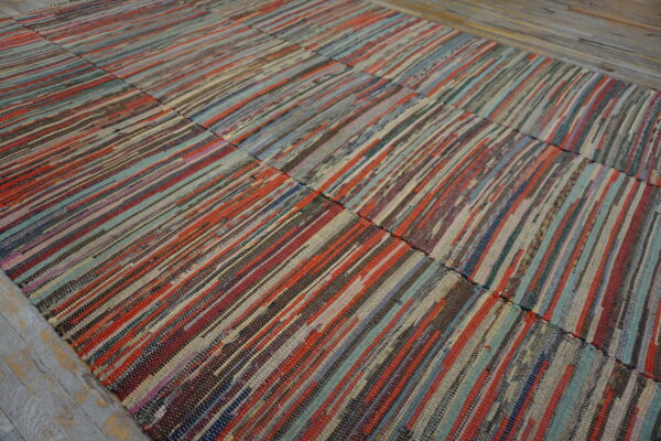 Multicolored flatweave rag rug with thin vertical stripes in reds, blues, and browns on worn wooden flooring.