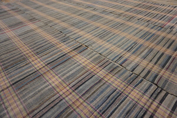 Flatwoven plaid rug in muted tones of blue, gray, and tan, accented with thin pink stripes.