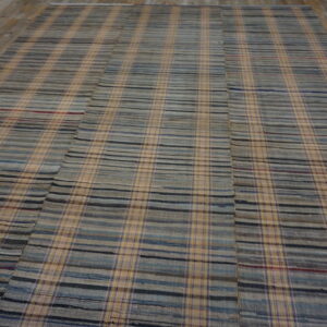 Flatwoven rug featuring a plaid pattern of gray, blue, and tan stripes on a worn wood floor.