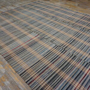 Pieced flatweave rug in gray and tan plaid stripes rests on distressed yellow and gray wood flooring.