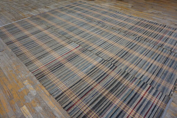 Pieced flatweave rug in gray and tan plaid stripes rests on distressed yellow and gray wood flooring.