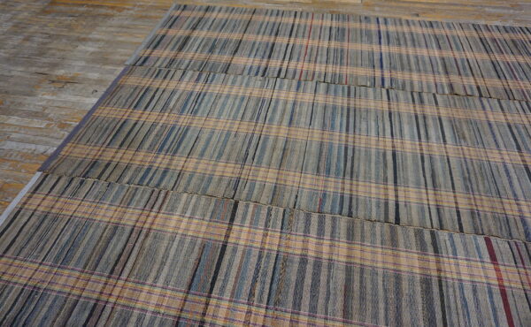 Muted gray, blue, and tan plaid rug assembled from woven panels, displayed on weathered wood planks.