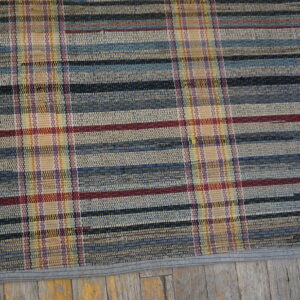 Multicolored flat weave rug featuring a plaid pattern resting on distressed wood floor.