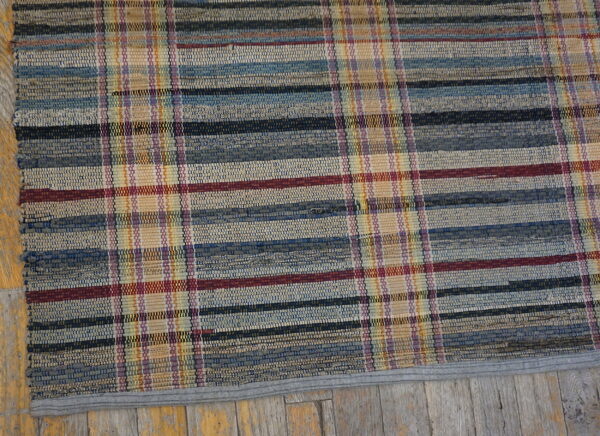 Multicolored flat weave rug featuring a plaid pattern resting on distressed wood floor.