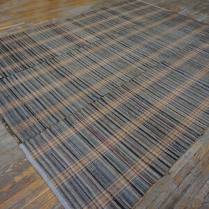Low-profile plaid rug in muted blues, grays, and beige rests on worn hardwood flooring.