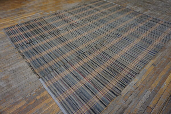 Low-profile plaid rug in muted blues, grays, and beige rests on worn hardwood flooring.