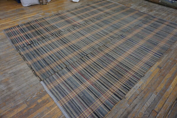 Flat-woven plaid rug with tan, gray, and blue stripes lying on rustic, multi-toned wood flooring.