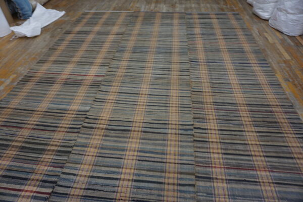 Low-pile blue, gray, and tan plaid rug assembled from panels, laid on worn wooden plank flooring.