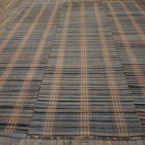 Low profile rug featuring a large plaid pattern in muted gray, tan, blue, and black stripes.