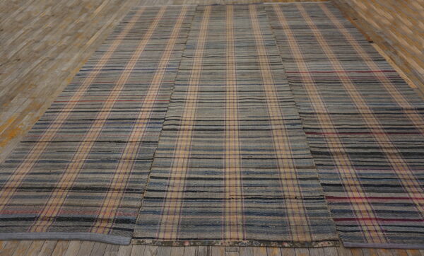 Low profile rug featuring a large plaid pattern in muted gray, tan, blue, and black stripes.