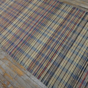 Multicolor flatweave rug with plaid stripes in blue, red, and yellow, laid over weathered gray wood flooring.