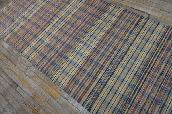 Multicolor flatweave rug with plaid stripes in blue, red, and yellow, laid over weathered gray wood flooring.
