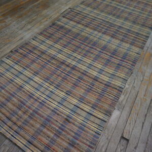 Muted blue, beige, and red striped flatweave runner lies diagonally on distressed wooden planks.