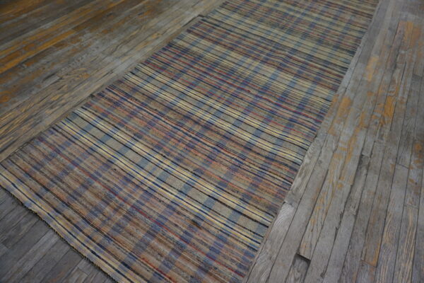 Muted blue, beige, and red striped flatweave runner lies diagonally on distressed wooden planks.
