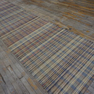 Flatweave runner rug with a multicolored plaid pattern lies on distressed gray wood floorboards.