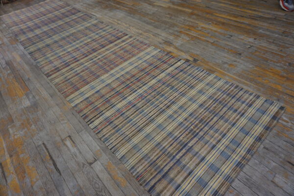 Flatweave runner rug with a multicolored plaid pattern lies on distressed gray wood floorboards.