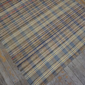 Variegated plaid rug in blues, yellows, and browns covers weathered gray wood planks.