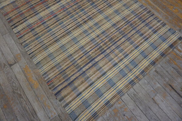 Variegated plaid rug in blues, yellows, and browns covers weathered gray wood planks.