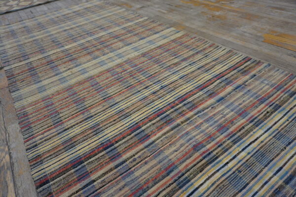 Rag rug with blue, red, yellow, and cream stripes lies on weathered wood floor.