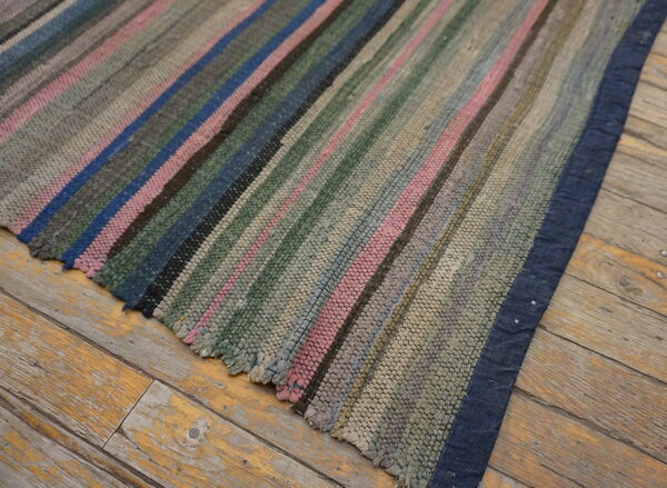 Faded pink, blue, and green striped woven rug with a dark blue border on distressed wood flooring.