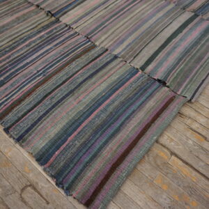 Flatweave patchwork rug with vertical stripes of grey, pink, and blue on distressed wooden floor.
