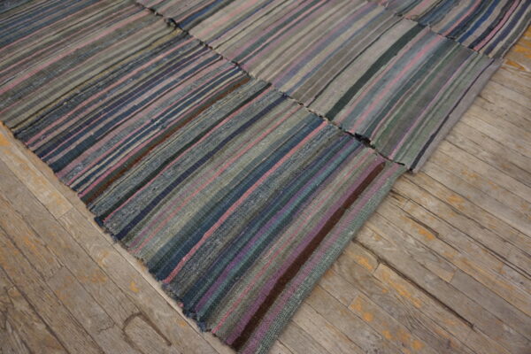 Flatweave patchwork rug with vertical stripes of grey, pink, and blue on distressed wooden floor.