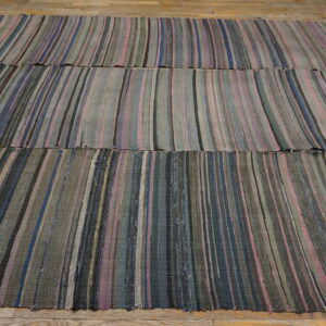 Flatweave rug with vertical stripes of blue, pink, gray, and green colors resting on wood planks.