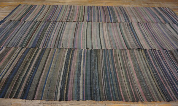 Flatweave rug with vertical stripes of blue, pink, gray, and green colors resting on wood planks.