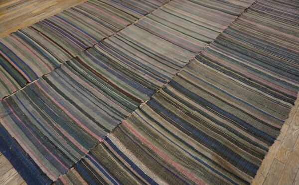 Striped, pieced flatweave rug in muted greens, blues, pinks, and grays lying on plank wood floor.