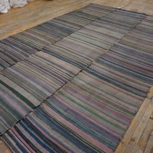 A large patched flatweave rug with thin stripes in muted grey, blue, pink, and green rests on wood floors.
