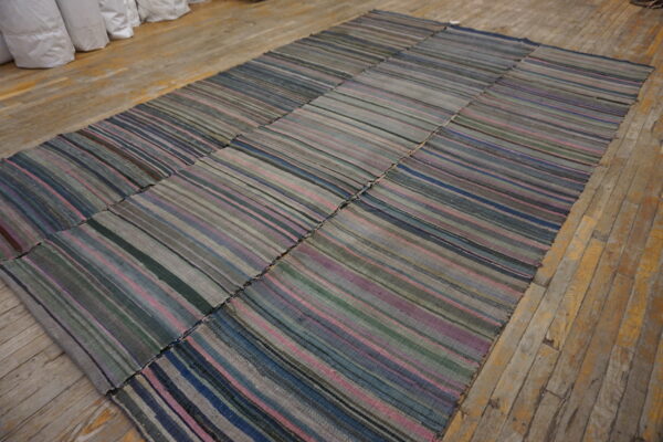 A large patched flatweave rug with thin stripes in muted grey, blue, pink, and green rests on wood floors.
