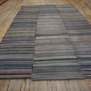 Muted striped flatweave rug sewn together from three panels rests on a distressed wooden floor.