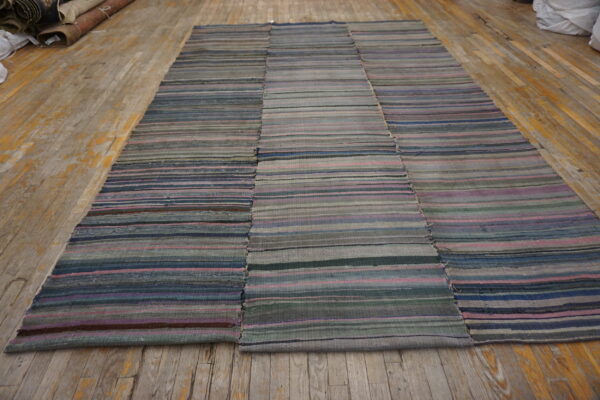 Muted striped flatweave rug sewn together from three panels rests on a distressed wooden floor.