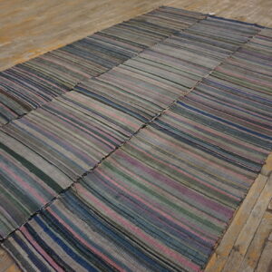 Muted patchwork flatweave rug featuring gray, blue, and mauve vertical stripes on worn wood flooring.