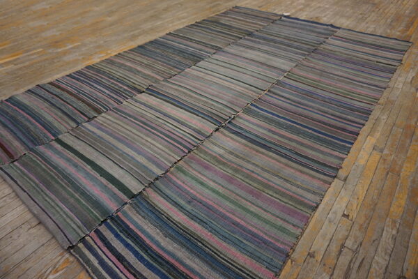 Muted patchwork flatweave rug featuring gray, blue, and mauve vertical stripes on worn wood flooring.