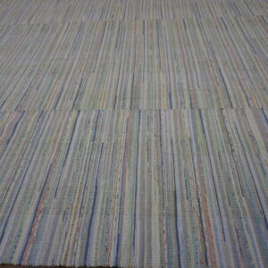 A large, flat-woven rag rug with vertical stripes in muted blue, cream, green, and pink tones rests on a wood floor.