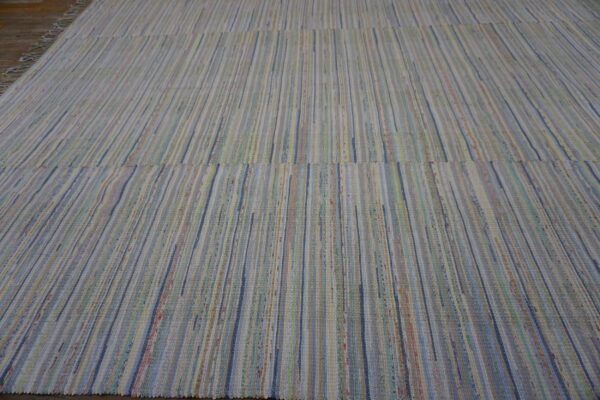A large, flat-woven rag rug with vertical stripes in muted blue, cream, green, and pink tones rests on a wood floor.