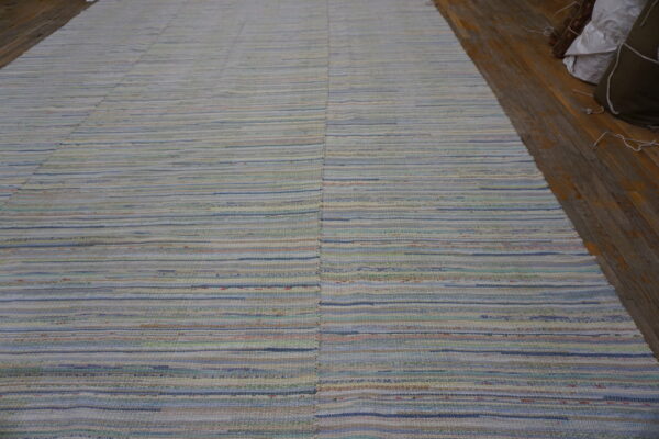 Lightly colored flatweave rug featuring thin horizontal stripes of blue, cream, green, and pink tones on wood flooring.